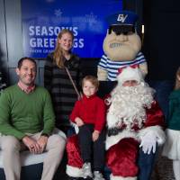 Parents with boy and girl smile sitting on Santa's lap with Louie standing
